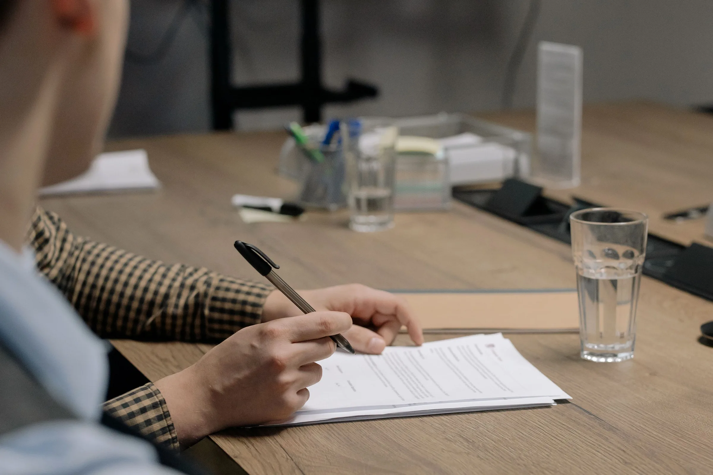 A person signing a multi-page printed contract with a pen at a wooden table